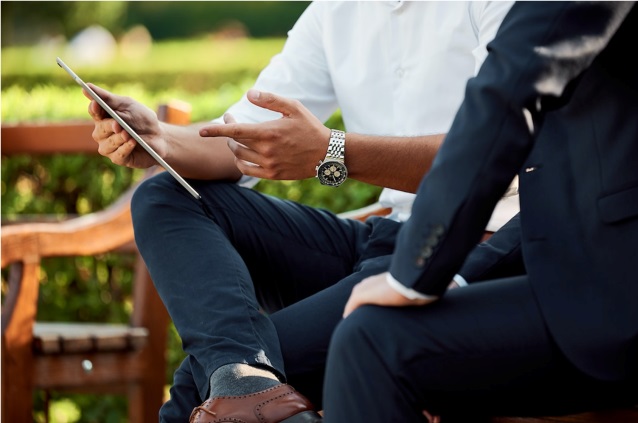 Two businessmen discussing what is capacity utilization and operating rate using a tablet device